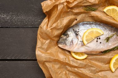 Koyu ahşap arka planda limonlu çiğ dorado balığı.