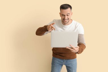 Bej arka planda dizüstü bilgisayarı gösteren mutlu genç adam.