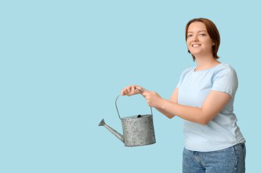 Mavi arka planda sulama tenekesi olan gülümseyen genç kadın.