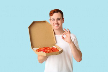Genç adam elinde lezzetli pizzayla karton kutu tutuyor ve mavi arka planda iyi görünüyor.