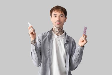 Burun damlası ve gri arka planda hapları olan alerjik genç bir adam.