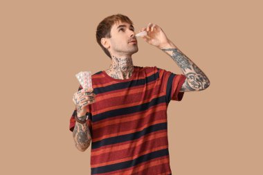 Kahverengi arka planda burun damlası kullanan alerjisi olan genç bir adam.