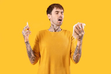 Burun damlası ve sarı arka planda hapşıran dokulara alerjisi olan genç bir adam.