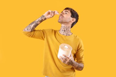 Sarı arka planda burun damlası kullanan, dokuları olan alerjik genç bir adam.