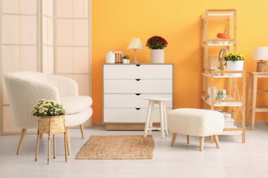 Beyaz kanepe ve hasırdan vazoda kasımpatı çiçekleri olan şık bir oturma odası.