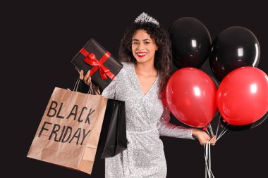 Alış veriş torbaları, balonlar ve karanlık arka planda hediye kutusuyla güzel bir Afro-Amerikalı kadın. Kara Cuma indirimi