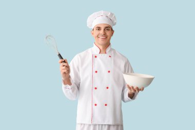 Mavi arka planda kâsesi ve çırpışı olan yakışıklı, mutlu bir aşçı.