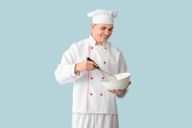 Mavi arka planda kâsesi ve çırpışı olan yakışıklı, mutlu bir aşçı.