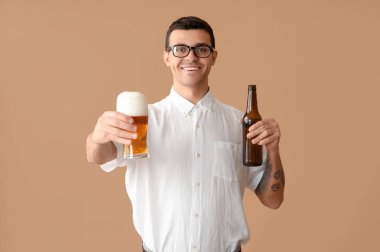 Kahverengi arka planda şişe ve bir bardak birası olan yakışıklı genç adam.
