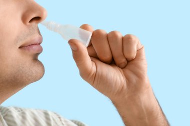 Mavi arka planda burun damlası kullanan genç adam, yakın plan.