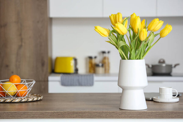 Vase with yellow tulip flowers on wooden table in modern kitchen
