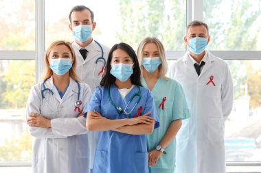 Kliniğin penceresinin yanında maskeli ve kırmızı kurdeleli profesyonel doktorlar. Dünya AIDS Günü konsepti