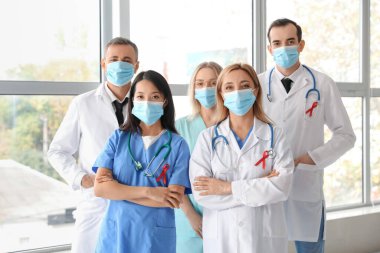 Kliniğin penceresinin yanında maskeli ve kırmızı kurdeleli profesyonel doktorlar. Dünya AIDS Günü konsepti