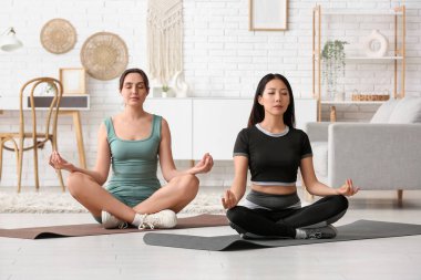 Spor yapan genç kadınlar evde meditasyon yapıyorlar.