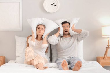 Yatak odasındaki gürültücü komşulardan muzdarip yastıklı genç bir çift.
