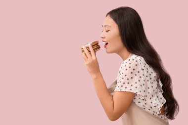 Genç Asyalı kadın pembe arka planda lezzetli krepler yiyor.