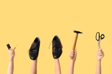 Sarı arka planda ayakkabı, çekiç ve el işi aletleri olan kadın eller. Ayakkabı tamiri kavramı