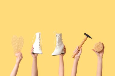 Sarı arka planda çizmeli, çekiçli ve tabanlı kadın elleri var. Ayakkabı tamiri kavramı