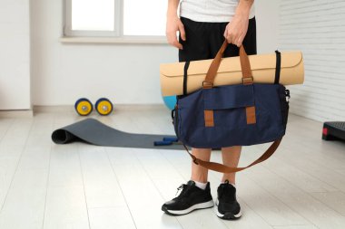 Spor çantası ve yoga minderiyle spor salonunda genç bir adam.