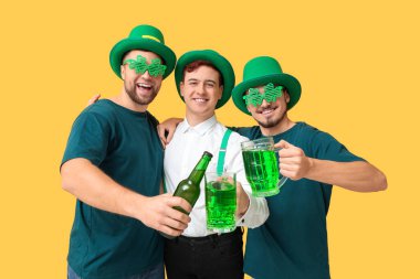 Leprikon şapkalı mutlu genç adamlar ve sarı arka planda bira. Aziz Patrick Günü kutlaması