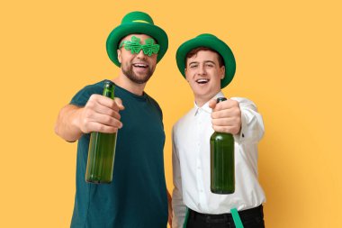 Sarı arka planda bira şişeleri olan cüce şapkalı mutlu genç adamlar. Aziz Patrick Günü kutlaması