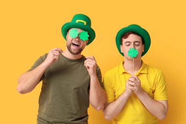 Sarı arka planda yoncalar olan cüce şapkalı komik genç adamlar. Aziz Patrick Günü kutlaması