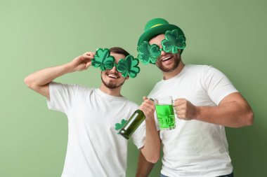 Parti bardakları ve yeşil arka planda biraları olan mutlu genç adamlar. Aziz Patrick Günü kutlaması