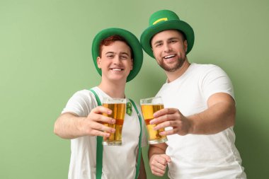 Yeşil arka planda bira bardakları olan cüce şapkalı mutlu genç adamlar. Aziz Patrick Günü kutlaması