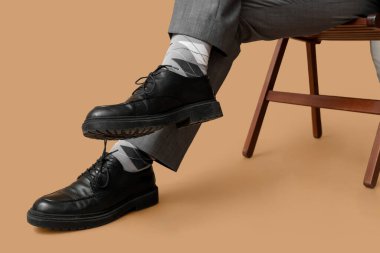 Kahverengi arka planda siyah şık ayakkabılı genç adamın bacakları.