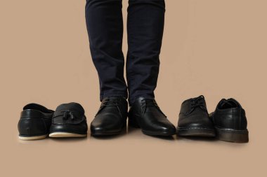 Kahverengi arka planda farklı siyah ayakkabıları olan genç bir adamın bacakları.