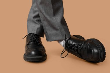 Kahverengi arka planda siyah şık ayakkabılı genç adamın bacakları.