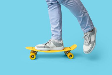 Mavi arka planda kaykaylı şık spor ayakkabılı genç adam bacakları.