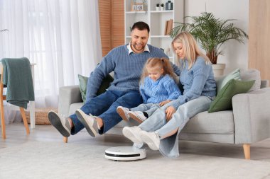 Evde robot elektrikli süpürgeyle ayaklarını kaldıran mutlu bir aile.