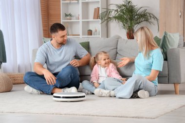 Evde halının üzerinde oturan elektrikli süpürgeli mutlu bir aile.
