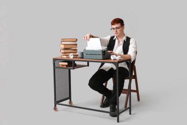 Klasik daktilosu ve gri arkaplanda kitapları olan genç bir adam.