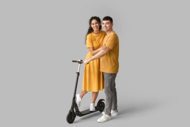 Gri arka planda modern elektrikli scooter kullanan mutlu genç bir çift.