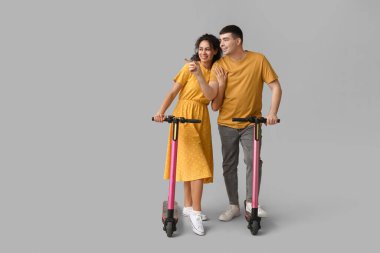 Gri arka planda modern elektrikli scooterları olan güzel genç bir çift.
