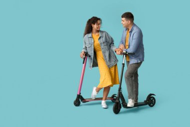 Mavi arka planda modern elektrikli scooterları olan güzel genç bir çift.
