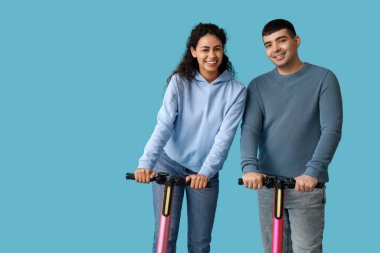 Mavi arka planda modern elektrikli scooterları olan mutlu genç çift.