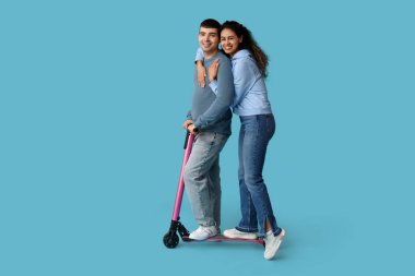 Mavi arka planda modern elektrikli scooter kullanan güzel genç bir çift.