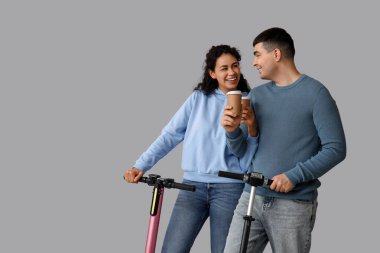 Modern elektrikli scooterları ve gri arka planda kağıt kahve fincanları olan güzel bir çift.