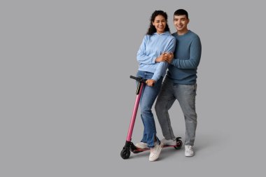 Gri arka planda modern elektrikli scooter kullanan mutlu genç bir çift.