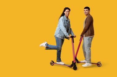 Sarı arka planda modern elektrikli scooter kullanan güzel genç bir çift.