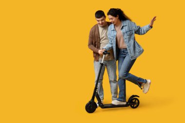Sarı arka planda modern elektrikli scooter kullanan güzel genç bir çift.