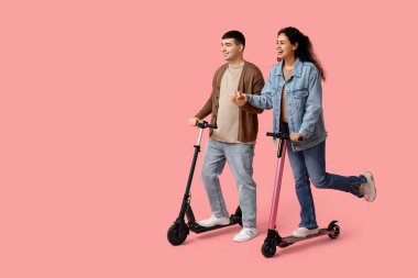 Pembe arka planda modern elektrikli scooter kullanan güzel bir çift.