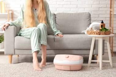 Masaj banyosu ve spa malzemeleri olan bir kadın evdeki kanepede oturuyor.