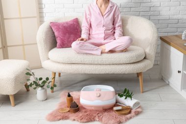 Kadın kanepede dinleniyor, ayak masajı yapıyor ve spa malzemeleri evde.