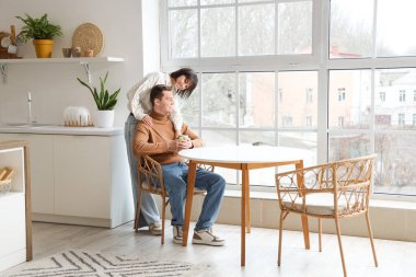 Genç bir kadın mutfakta kocasına bir fincan kahveyle sarılıyor.