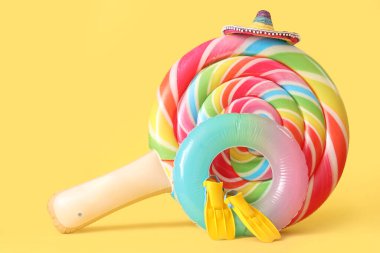 Şeker şeklinde yüzen yatak, şişirilebilir yüzük ve sarı arka planda paletler.