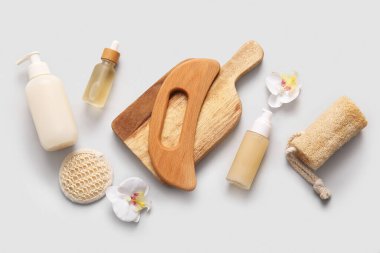 Ahşap guasha vücut masajı aleti, bir şişe serum ve gri arka planda yeniden kullanılabilir pamuk pedi olan kompozisyon